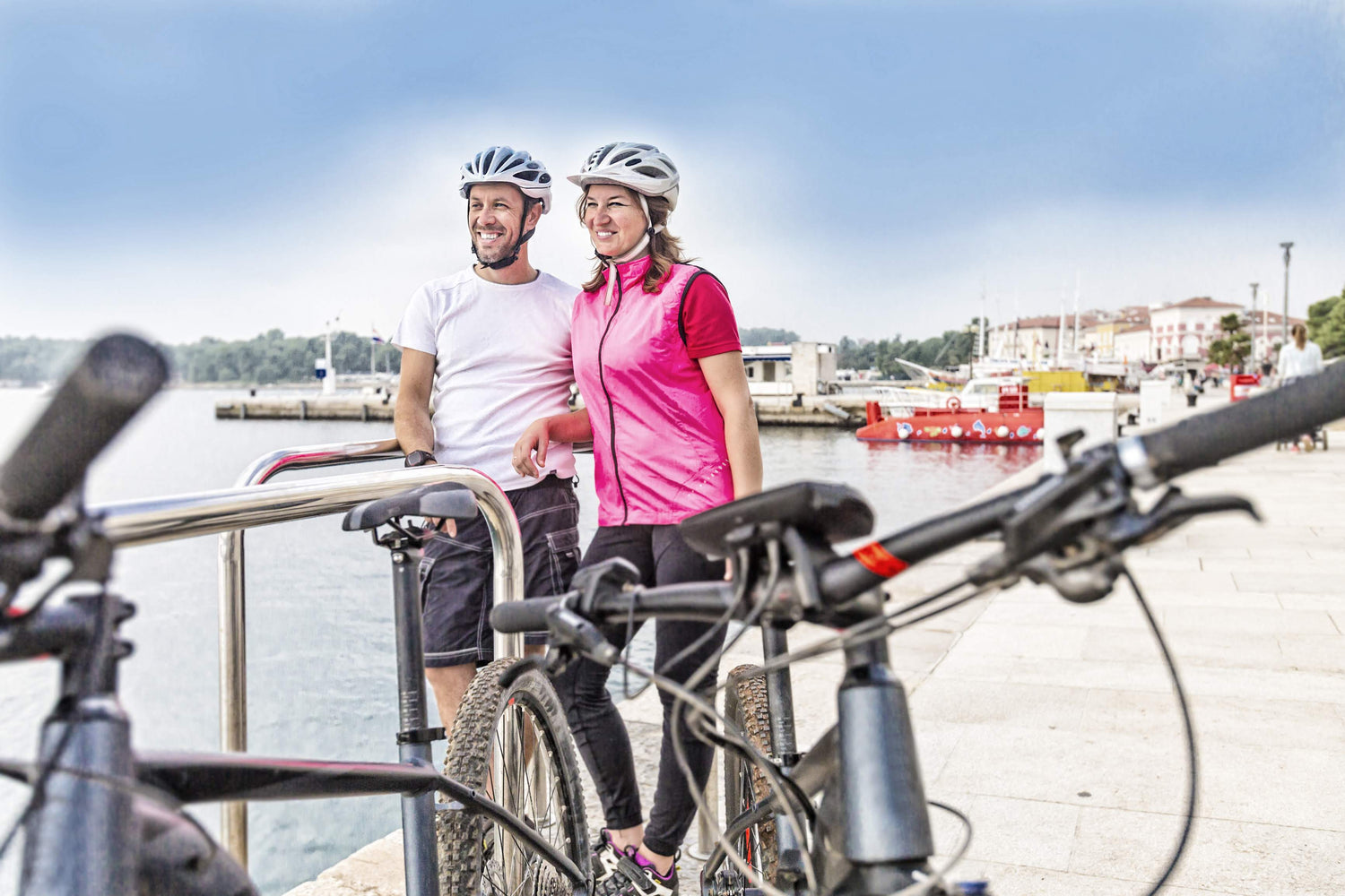 Mann und Frau mit Fahrradhelm und E-Bike am Wasser